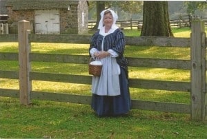 Bonnie Post in period clothing next to the barn.