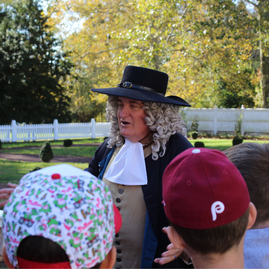 Man dressed as William Penn is talking outside to a pair of students on a field trip